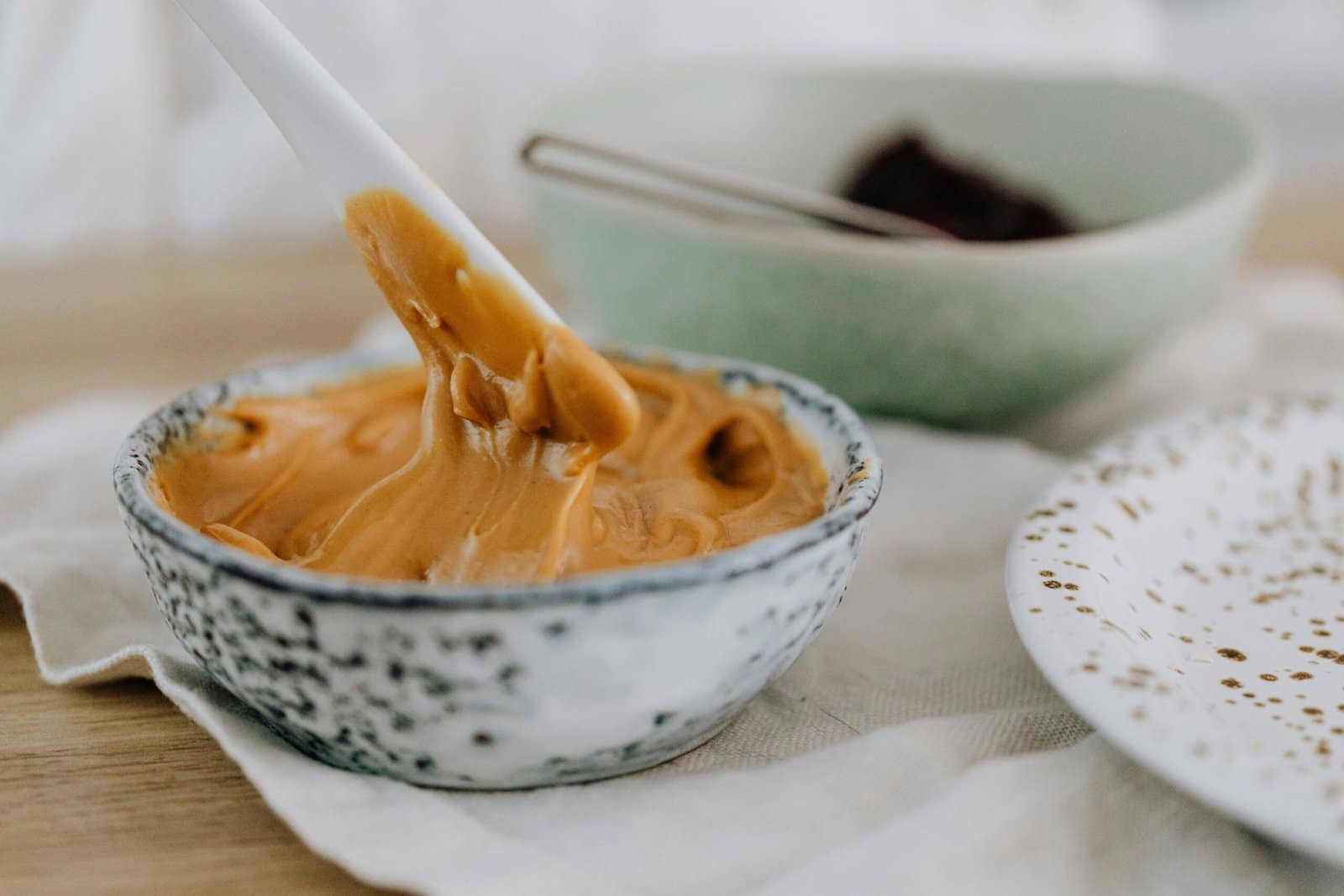 Close-up of creamy peanut butter swirled in a speckled ceramic bowl.