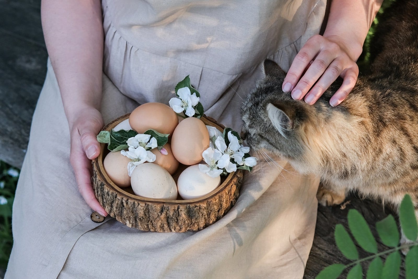 A woman holds a wooden plate with Easter eggs and caresses a cat. Easter in rustic style