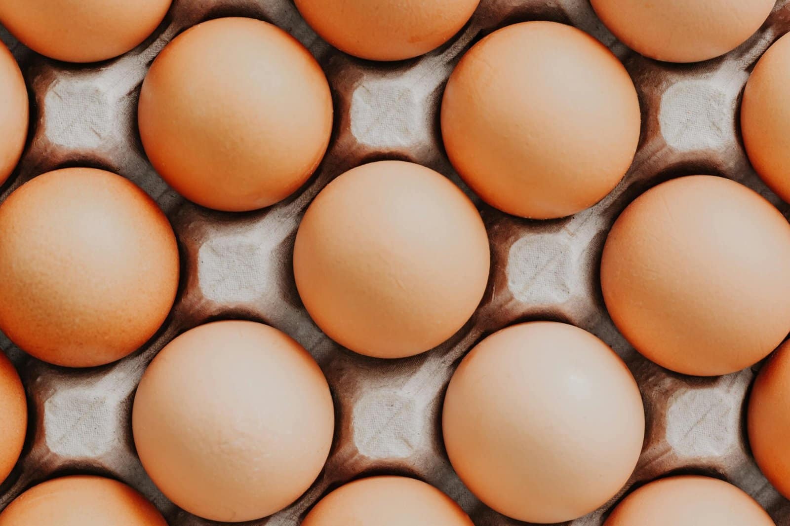 Overhead view of fresh brown eggs neatly arranged in a carton, showcasing their natural texture.