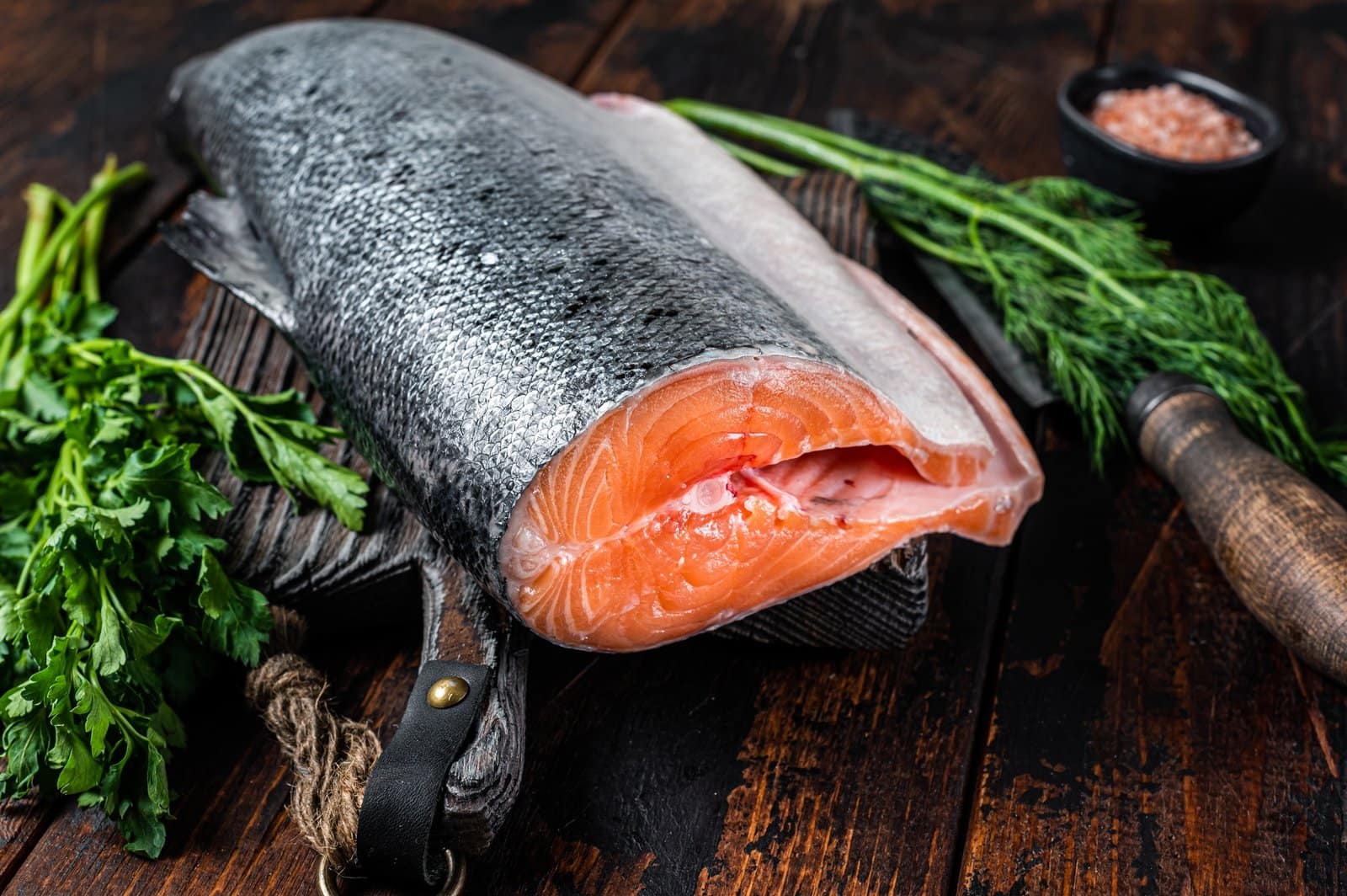 Big piece of Raw cut salmon fish on a wooden cutting board with chef knife.